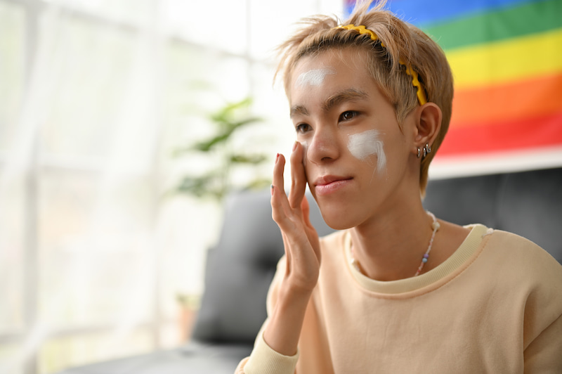 Happy young asian gay man is applying sunscreen or moisturizer on his face